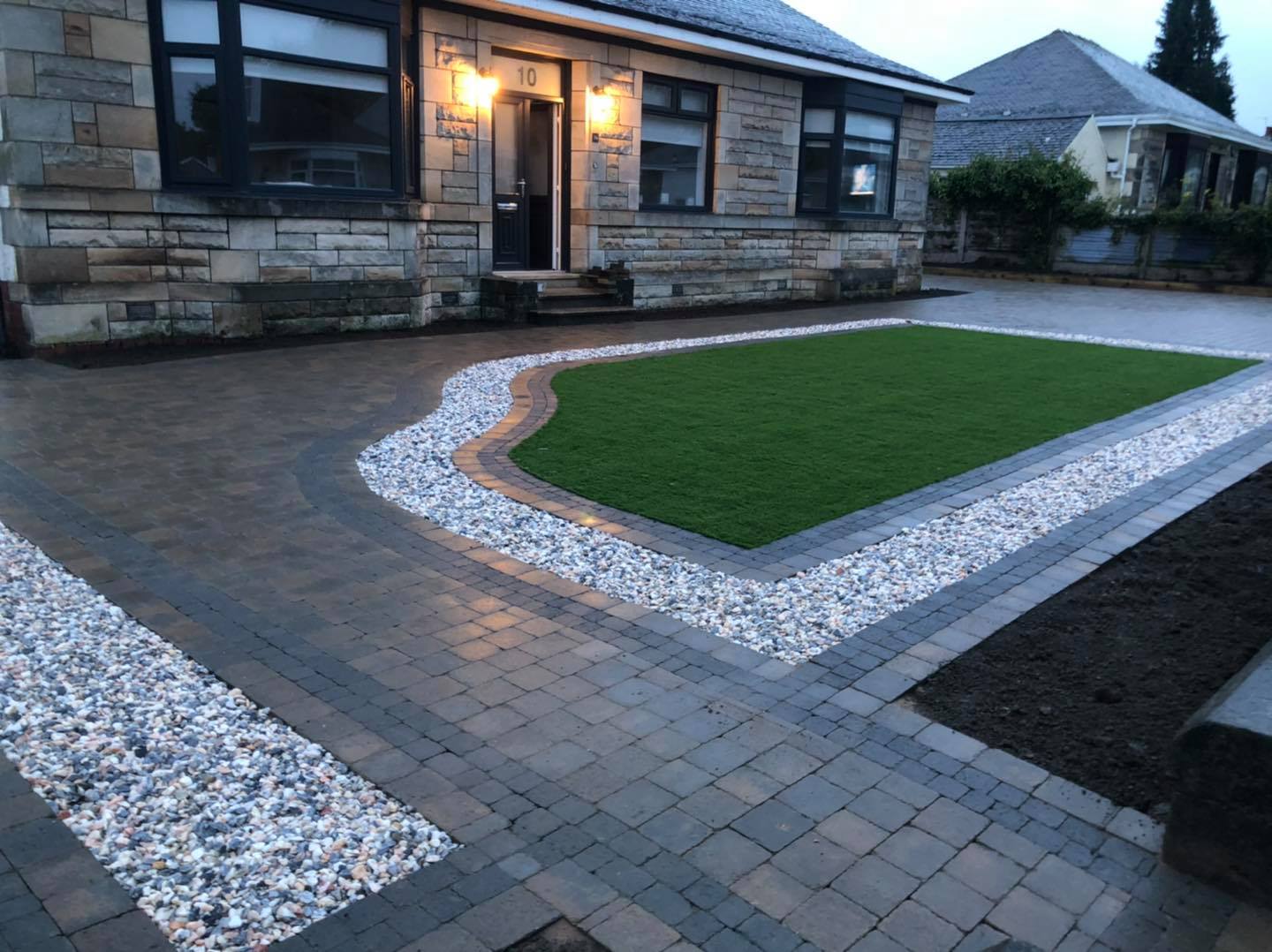 Tobermore tegular driveway installed with cobble setts as border, 40mm artificial grass installed, flower beds added with Flamingo decorative chips.