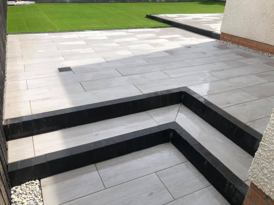 Finished Italian porcelain patio installed with matching paths, steps, artificial palm trees and artificial turf.